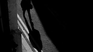 رجل يسير في شارع مظلم بينما يسبق ظلّه خطواته