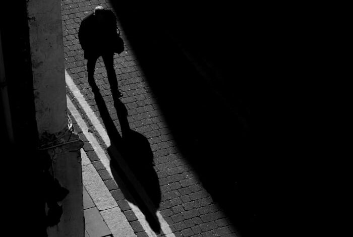 رجل يسير في شارع مظلم بينما يسبق ظلّه خطواته